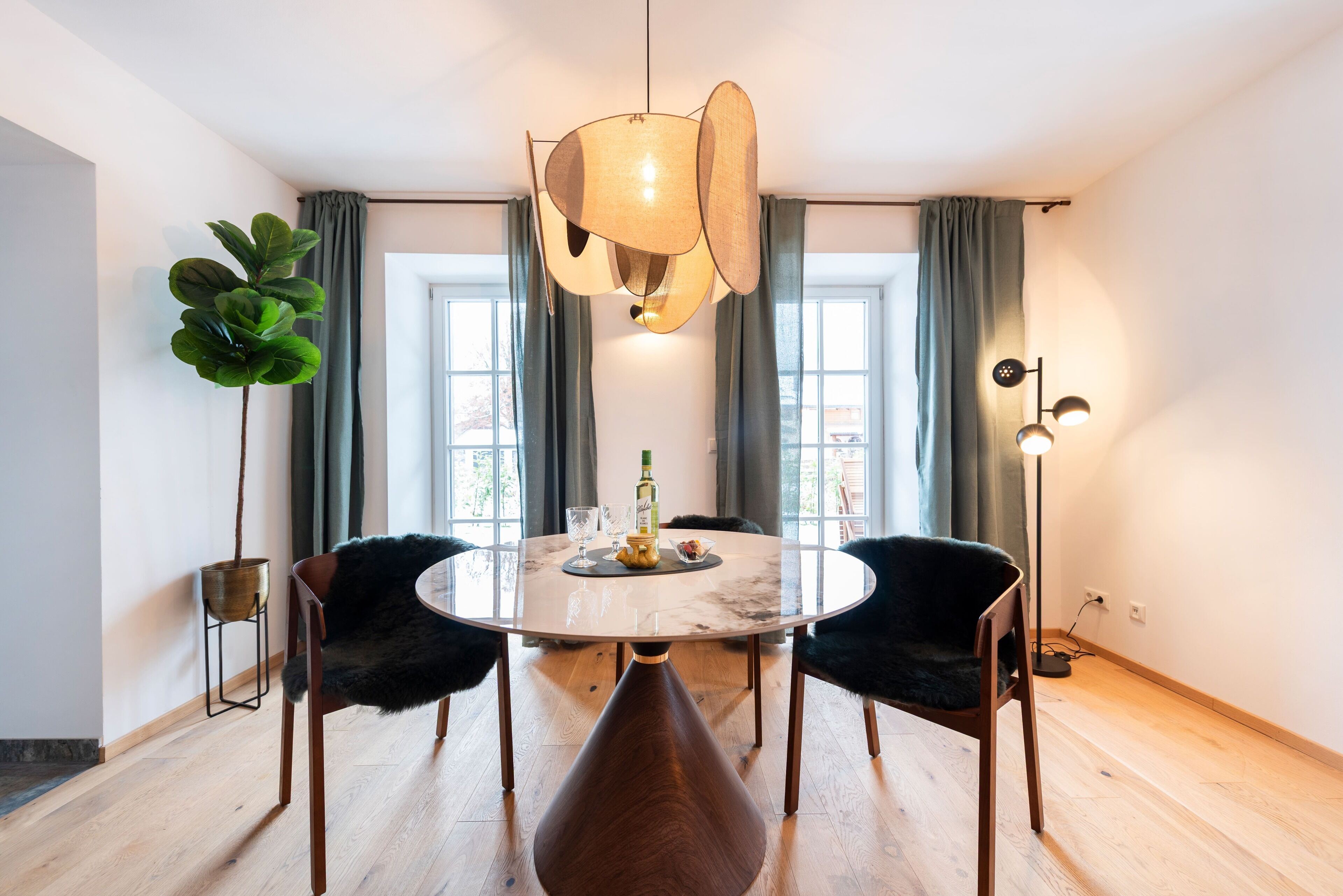 Een eethoek met een ronde tafel, twee stoelen, een hanglamp en een potplant.