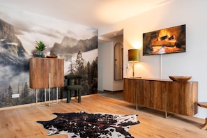 Een modern interieur met een houten vloer, een vachten vloerkleed, een houten kast, een spiegel en een muur met een berg- en vuurlandschap.