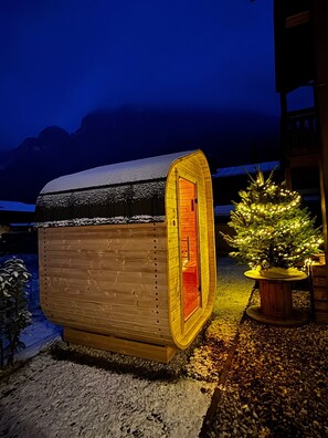 Een klein houten vakantiehuisje met een met sneeuw bedekte dak, een verlicht interieur en een kerstboom ervoor.