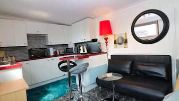 A compact living space with a kitchenette, a black leather sofa, a round table, and a red floor lamp.