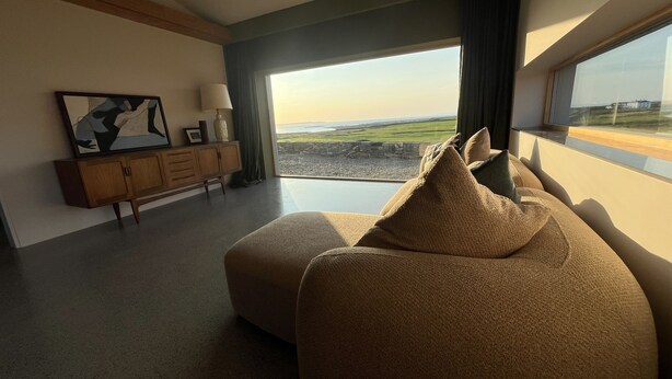 A modern living room with a large window, a sofa, a cabinet, and a painting on the wall.
