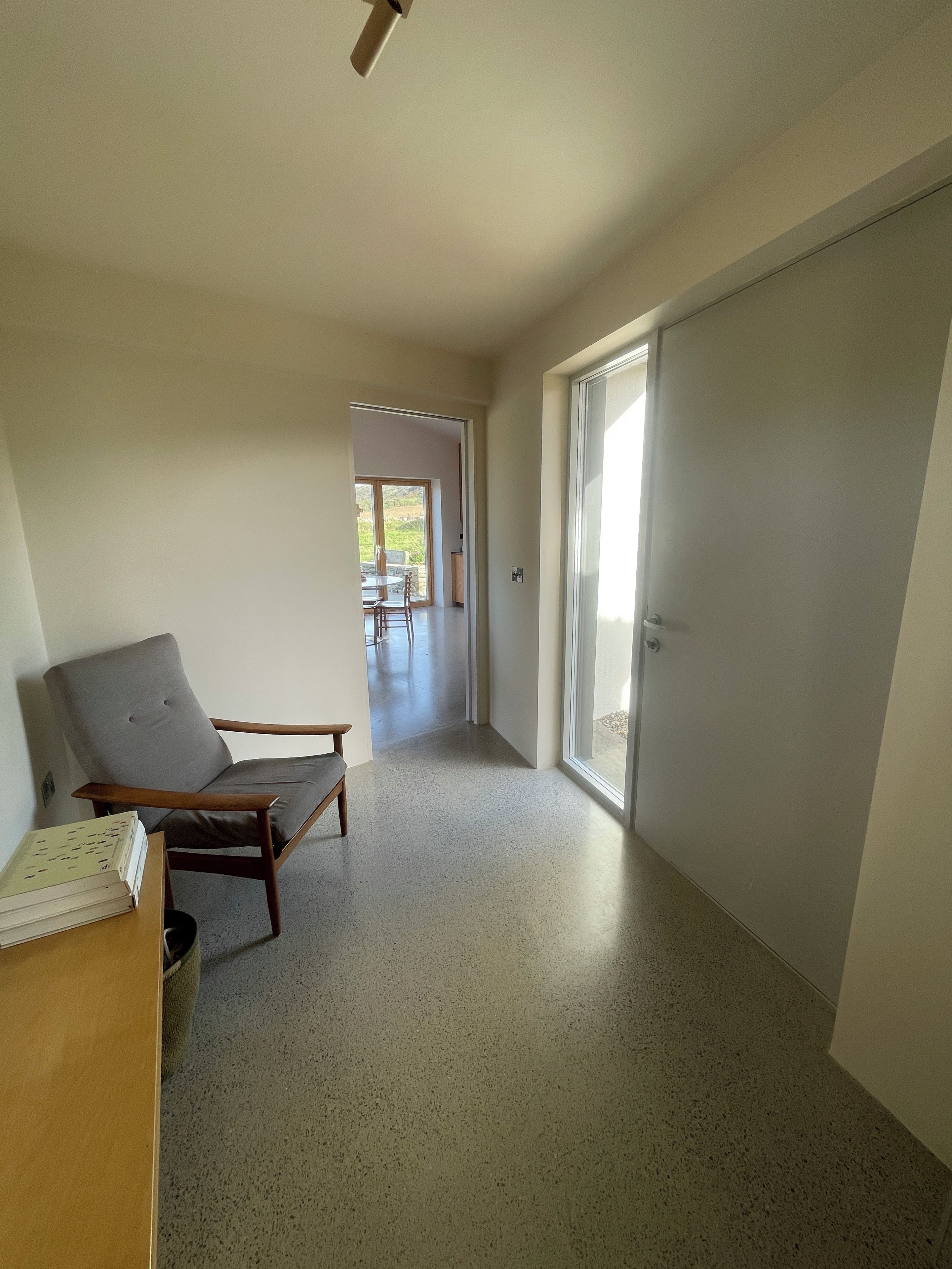 A hallway with a chair, a table with a book, and a door leading to a balcony.