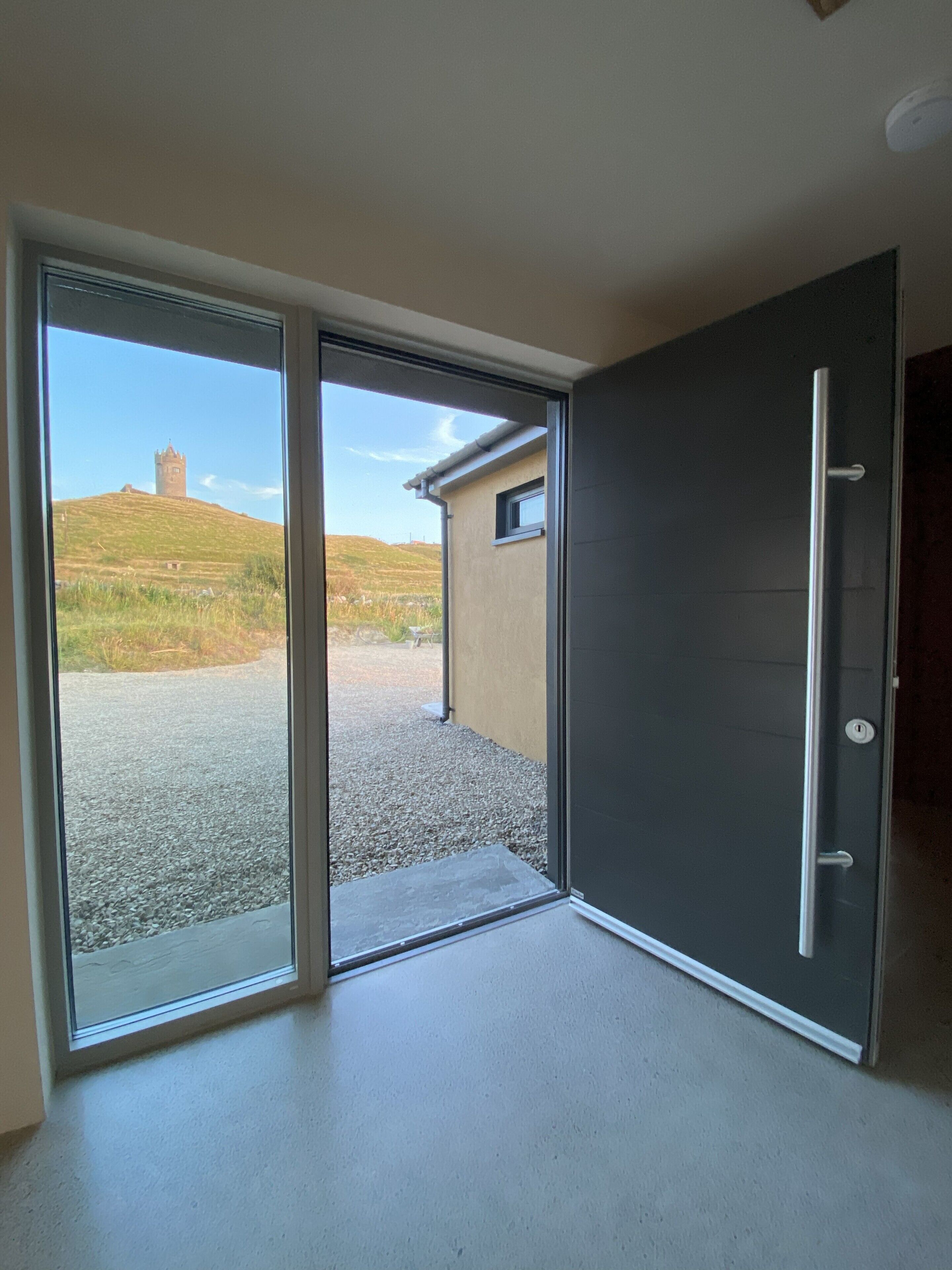 A room with a sliding glass door leading to an outdoor area with a gravel path and a hill with a tower.