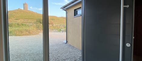 A room with a sliding glass door leading to an outdoor area with a gravel path and a hill with a tower.