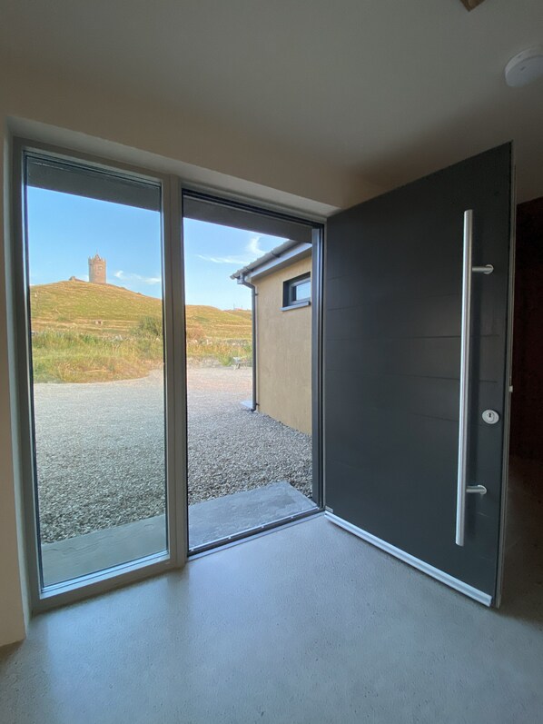 A room with a sliding glass door leading to an outdoor area with a gravel path and a hill with a tower.