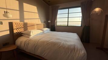 A bedroom with a large bed, a bedside table, a window with curtains, and a hanging light fixture.