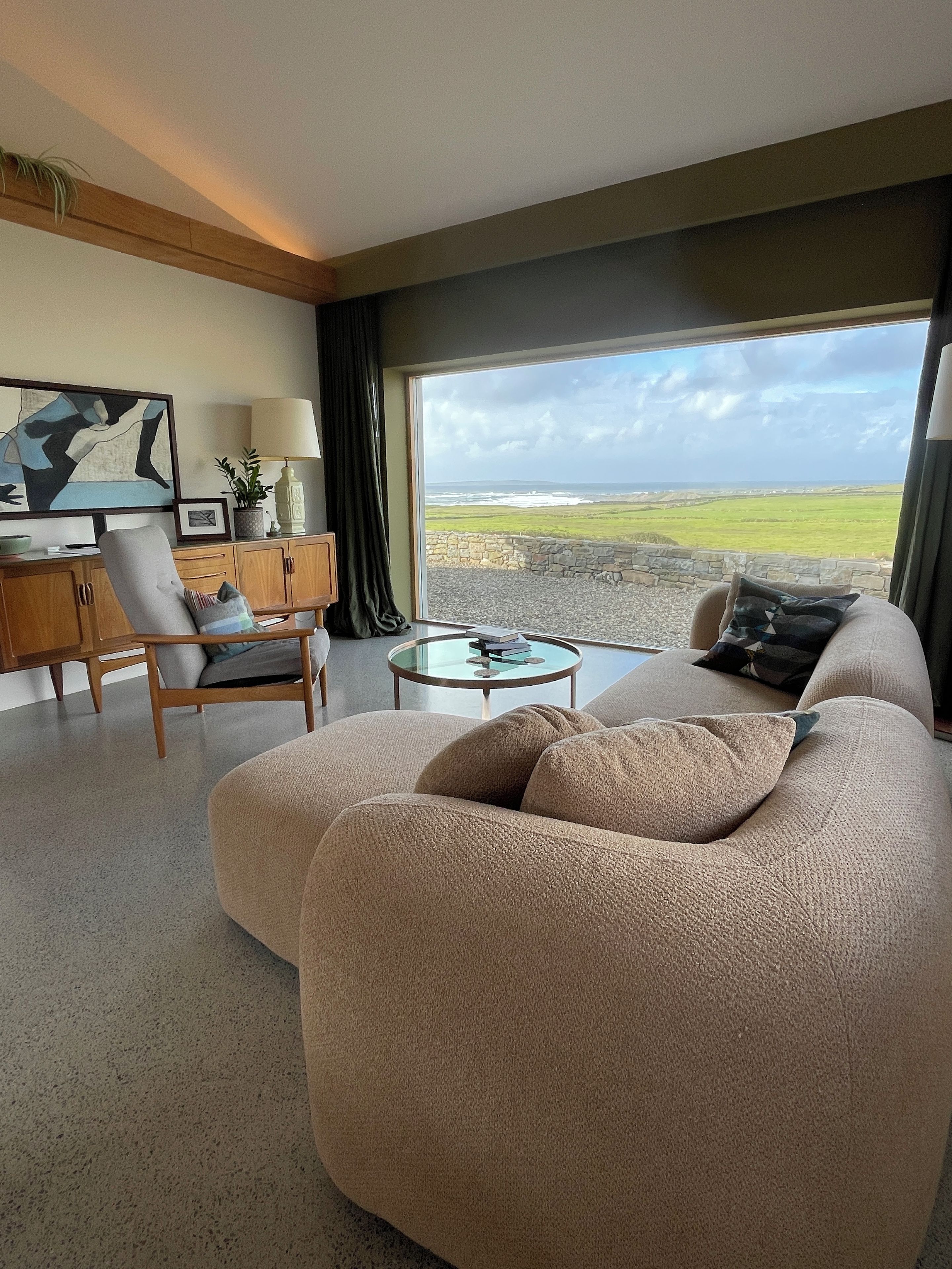 Un salón moderno con un sofá grande color beige, una mesa de centro de vidrio y vistas al campo.