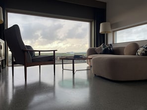 A modern living room with a large window, a sofa, a chair, and a coffee table.