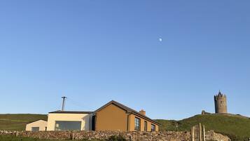 A rural landscape with a modern house, a stone wall, and a historic tower.