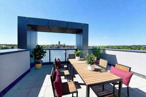 Eine Dachterrasse mit Holztisch und -stühlen, Topfpflanzen und Blick auf eine entfernte Skyline.