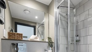 A modern bathroom with a white toilet, a sink, and a glass-enclosed shower. - Student Only Riverside (Canterbury)
