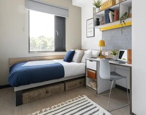 Ein Schlafzimmer mit Bett, Schreibtisch, Stuhl und Fenster.
