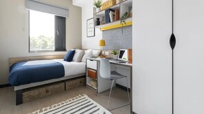Ein Schlafzimmer mit Bett, Schreibtisch, Stuhl und Fenster.