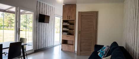 A modern living room with a sofa, a dining table with chairs, a built-in wooden shelving unit, and a sliding door.