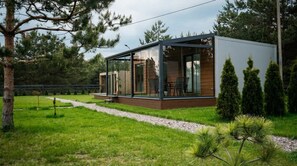 A modern cabin with a glass enclosure, wooden deck, and a surrounding garden.
