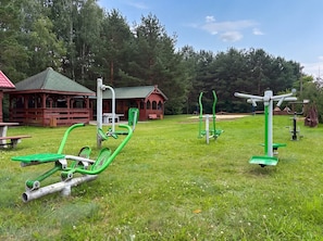 Outdoor exercise equipment in a park setting with a wooden cabin in the background.