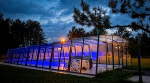 A transparent greenhouse structure with a glass roof, surrounded by trees.