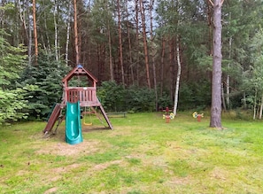 A playground with a slide and climbing structure surrounded by trees.