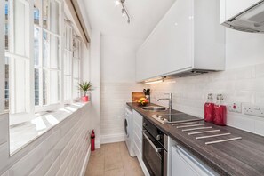 Eine moderne Küche mit weißen Schränken, einer dunklen Arbeitsplatte, einem eingebauten Backofen und einem Fenster mit einer Pflanze.