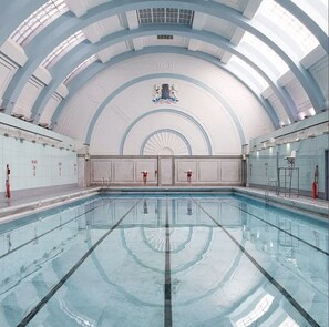Ein großes Hallenbad mit hoher, gewölbter Decke und einem zentralen Wappen.