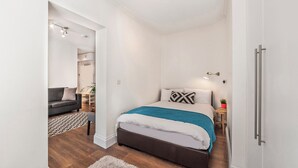 Een moderne slaapkamer met een groot bed, een grijze bank en een kleine tafel met een plant.