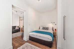 Ein modernes Schlafzimmer mit einem großen Bett, einem grauen Sofa und einem kleinen Tisch mit einer Pflanze.