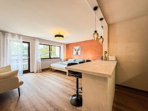 A modern room with a bed, a dining table, and a bar area. - ArgenZeit Vacation Rental – Centrally Located in Oberstaufen (Oberstaufen)