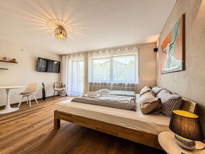 Une chambre à coucher avec un lit, une chaise, une table, un téléviseur et une fenêtre avec des rideaux.
