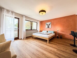 Un dormitori amb un llit de fusta, un radiador, una finestra amb cortines, una làmpada de paret i una cadira.