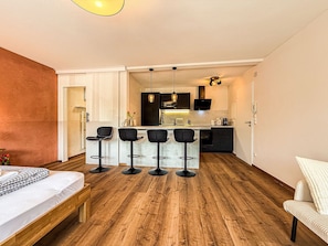 Une cuisine moderne avec un coin bar, un plancher en bois et un lit recouvert d’une courtepointe à carreaux.
