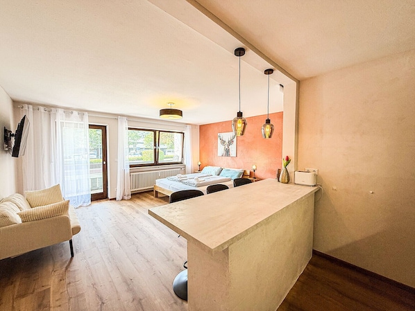 Une cuisine moderne avec un îlot central, un coin repas avec une table et des chaises, et un espace de vie avec un canapé et une fenêtre.