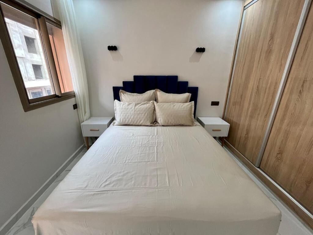 Un dormitorio con cama, mesitas de noche, un armario y una ventana.