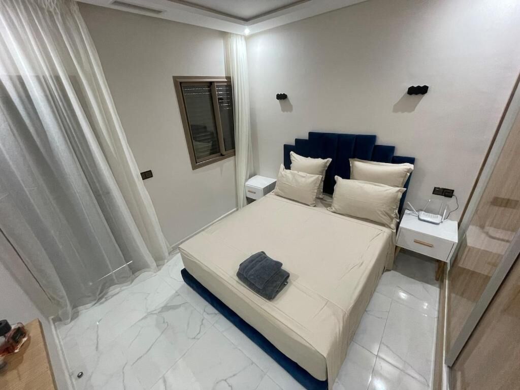 A hotel room with a bed, bedside tables, a window with curtains, and a nightstand.