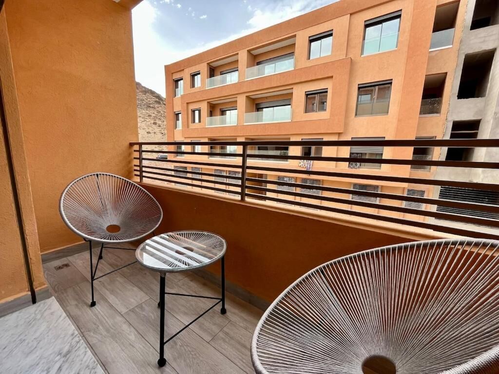Un balcon avec deux chaises et une petite table, donnant sur un immeuble doté de nombreux balcons.