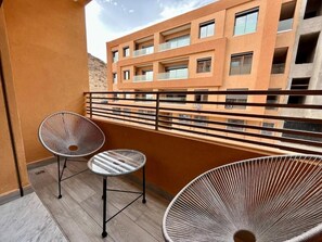 A balcony with two chairs and a small table, overlooking a building with multiple balconies. - Modern Stay City Center with Balcony (Marrakech)