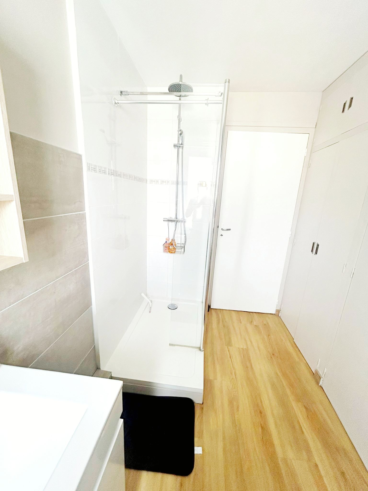 Une salle de bain moderne avec une douche à parois de verre, un lavabo blanc et un plancher en bois.