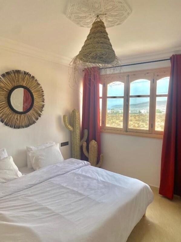 A bedroom with a bed, a large window, and a cactus decoration.