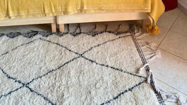 Una cama con una manta amarilla, una toalla enrollada y un tapete estampado.