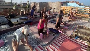 Un grupo de personas realizando actividad física en una azotea, con colchonetas de ejercicio y estructuras de madera.
