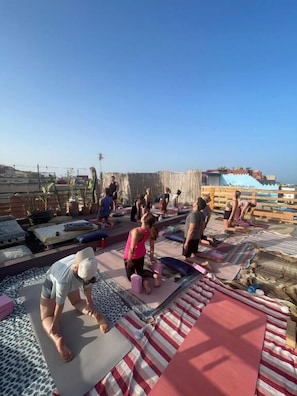 A group of people engaged in a physical activity on a rooftop with exercise mats and wooden structures. - Moana Surf Maroc (Aourir)