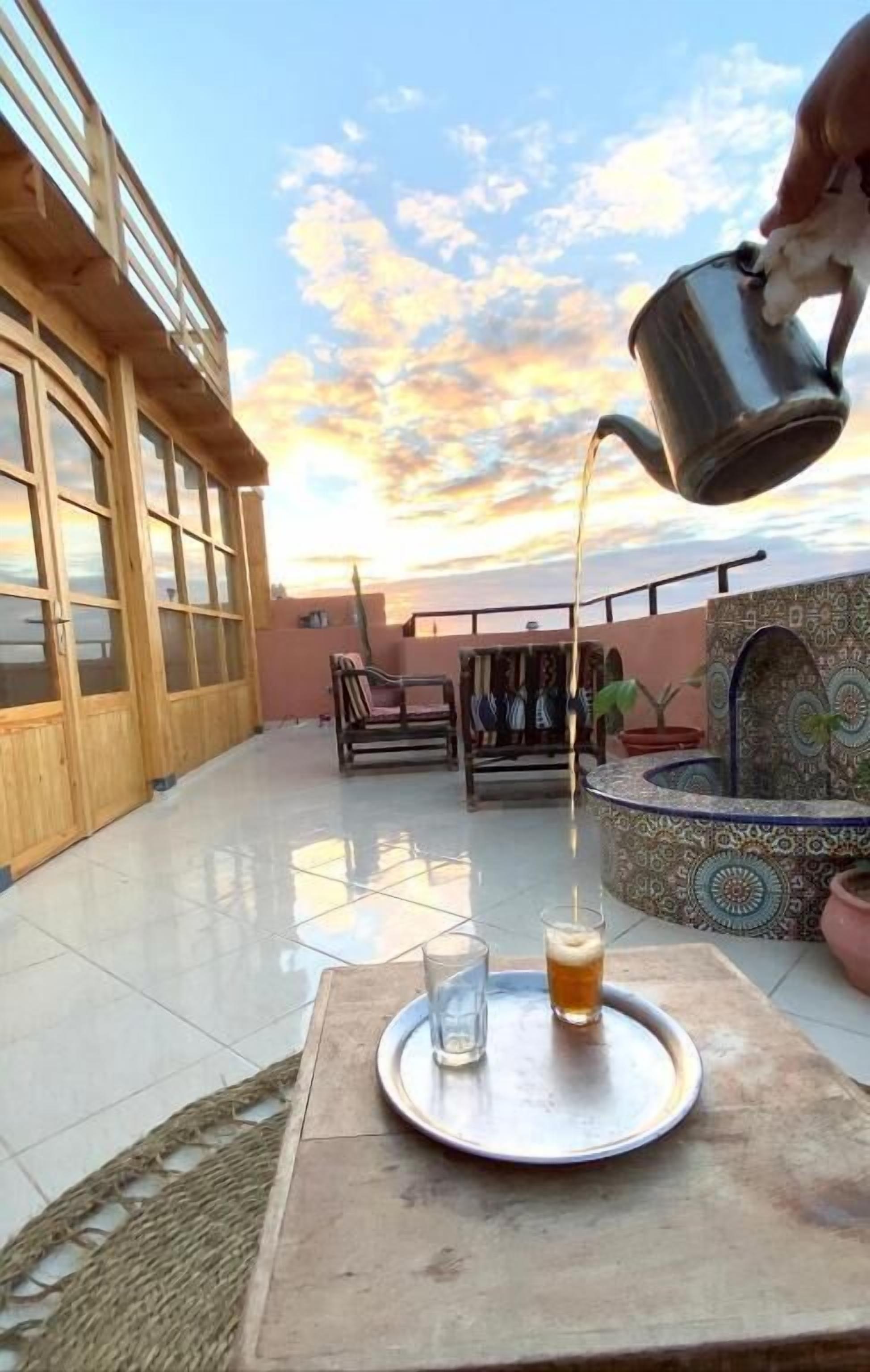 Un patio con una mesa lista para dos personas, una cerveza en un vaso y una jarra de metal sirviendo una bebida.