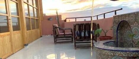 Un patio con una mesa lista para dos personas, una cerveza en un vaso y una jarra de metal sirviendo una bebida.