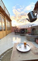 Un patio con una mesa lista para dos personas, una cerveza en un vaso y una jarra de metal sirviendo una bebida.