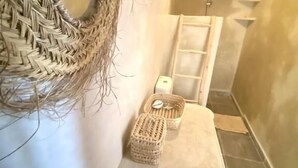 Un baño con un adorno tejido en la pared, una pequeña cesta tejida, una toalla y un lavabo estampado.