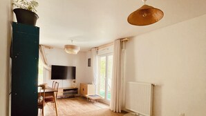 Ein Zimmer mit Esstisch, Stühlen, einer Couch, einem Fernseher und einer Heizung.