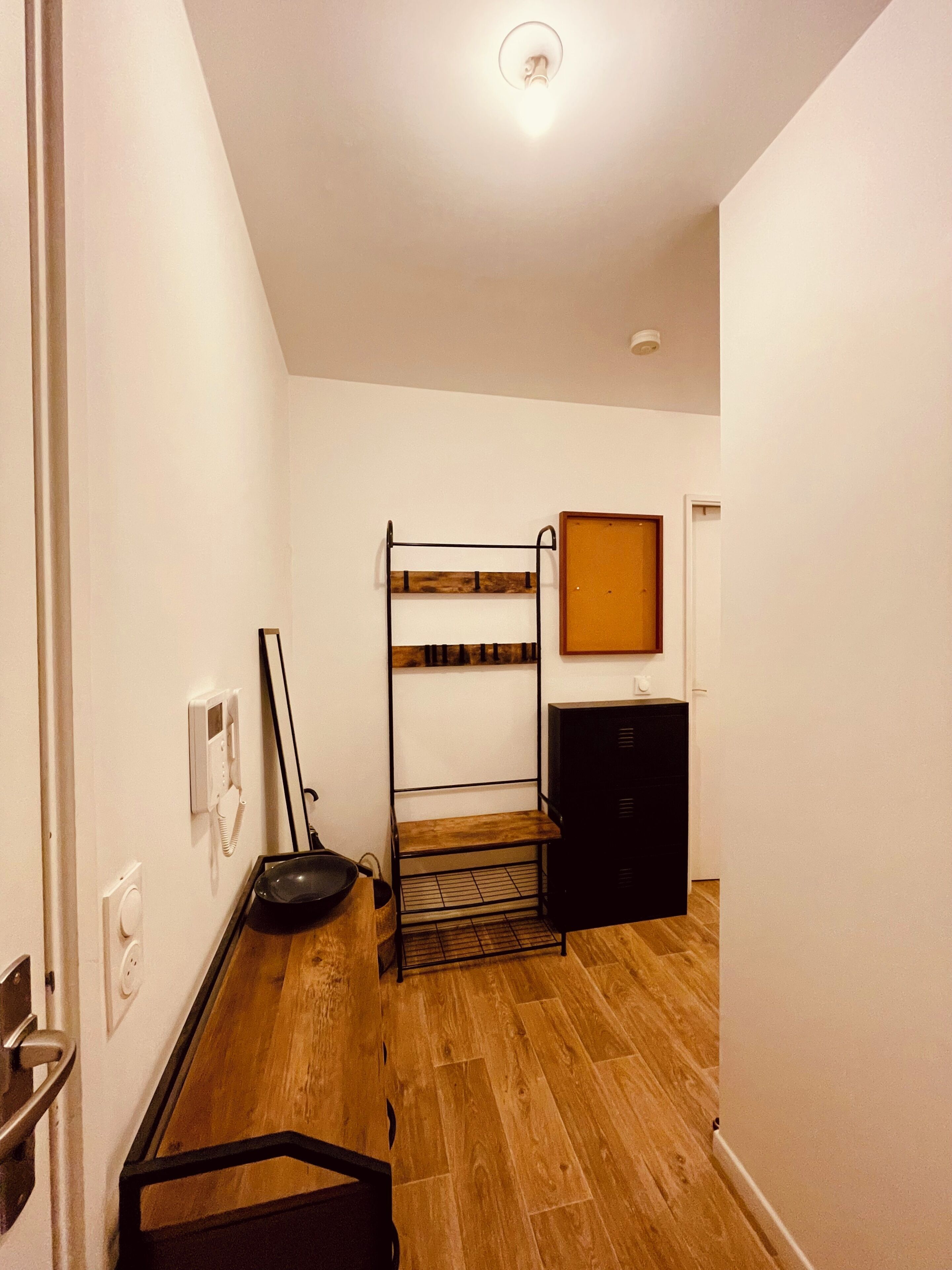 Une pièce avec un lit superposé, une petite armoire, une étagère fixée au mur et une porte dotée d’une poignée.