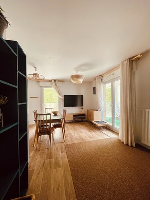 A spacious living area with a dining table, chairs, a flat-screen TV, and a large window with curtains. - A cozy and spacious apartment just outside Paris. Perfect for families. (Noisy-le-Sec)
