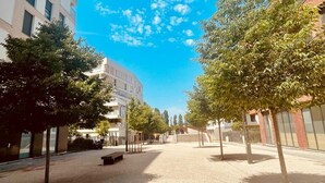 Ein weitläufiger Stadtplatz mit Bäumen, Bänken und modernen Gebäuden.