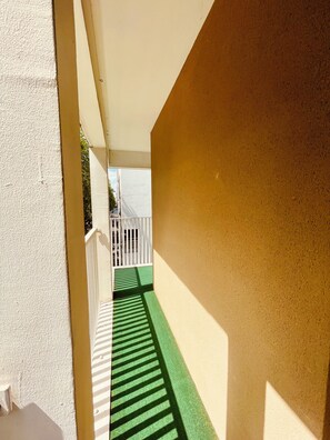 A narrow corridor with a green mat, white railing, and a view of a white fence and trees in the distance. - A cozy and spacious apartment just outside Paris. Perfect for families. (Noisy-le-Sec)