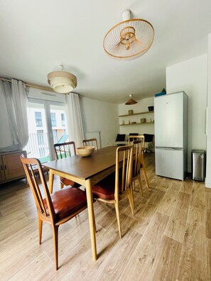 A dining area with a wooden table and chairs, a hanging light fixture, and a refrigerator. - A cozy and spacious apartment just outside Paris. Perfect for families. (Noisy-le-Sec)